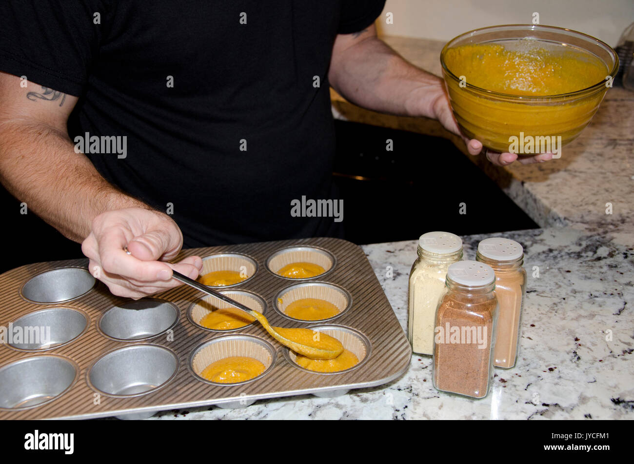 Close up of man baking pumpkin muffins at home for the holidays. Photo only shows the waist to neck no face is shown. Stock Photo