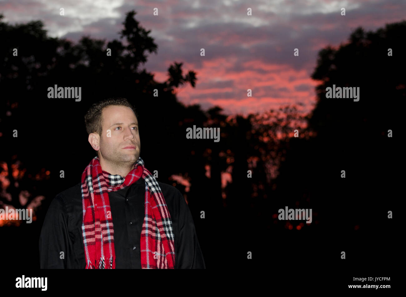 Man alone outside on a winter night wearing a scarf at sunset looking up and off to the side. Hopeful of what the New Year will bring. Stock Photo