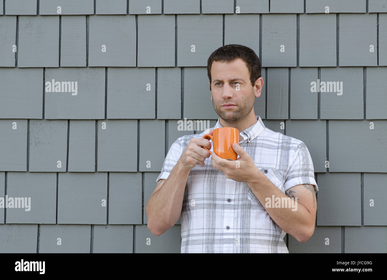 Man holding an orange coffee cup with two hands with a gray background. Stock Photo