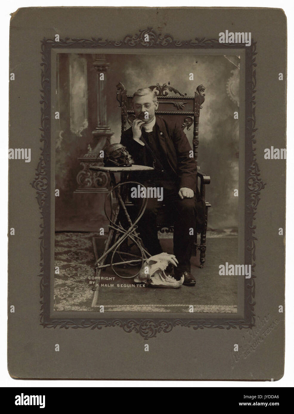Seated man, skulls on table and floor Stock Photo