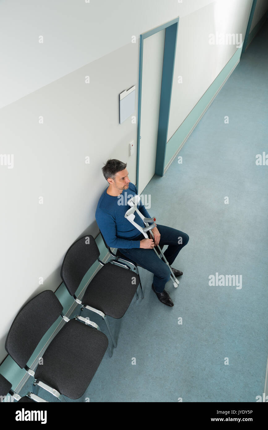 High Angle View Of A Man Sitting On Chair With Crutches In Hospital