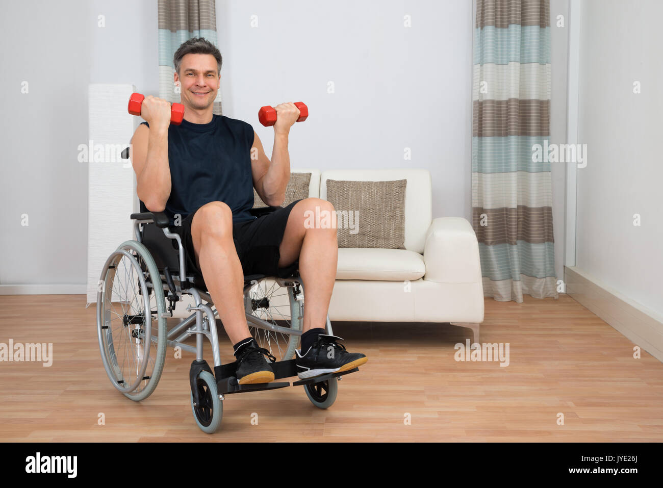 Handicapped Man On Wheelchair Working Out With Dumbbell At Home Stock Photo