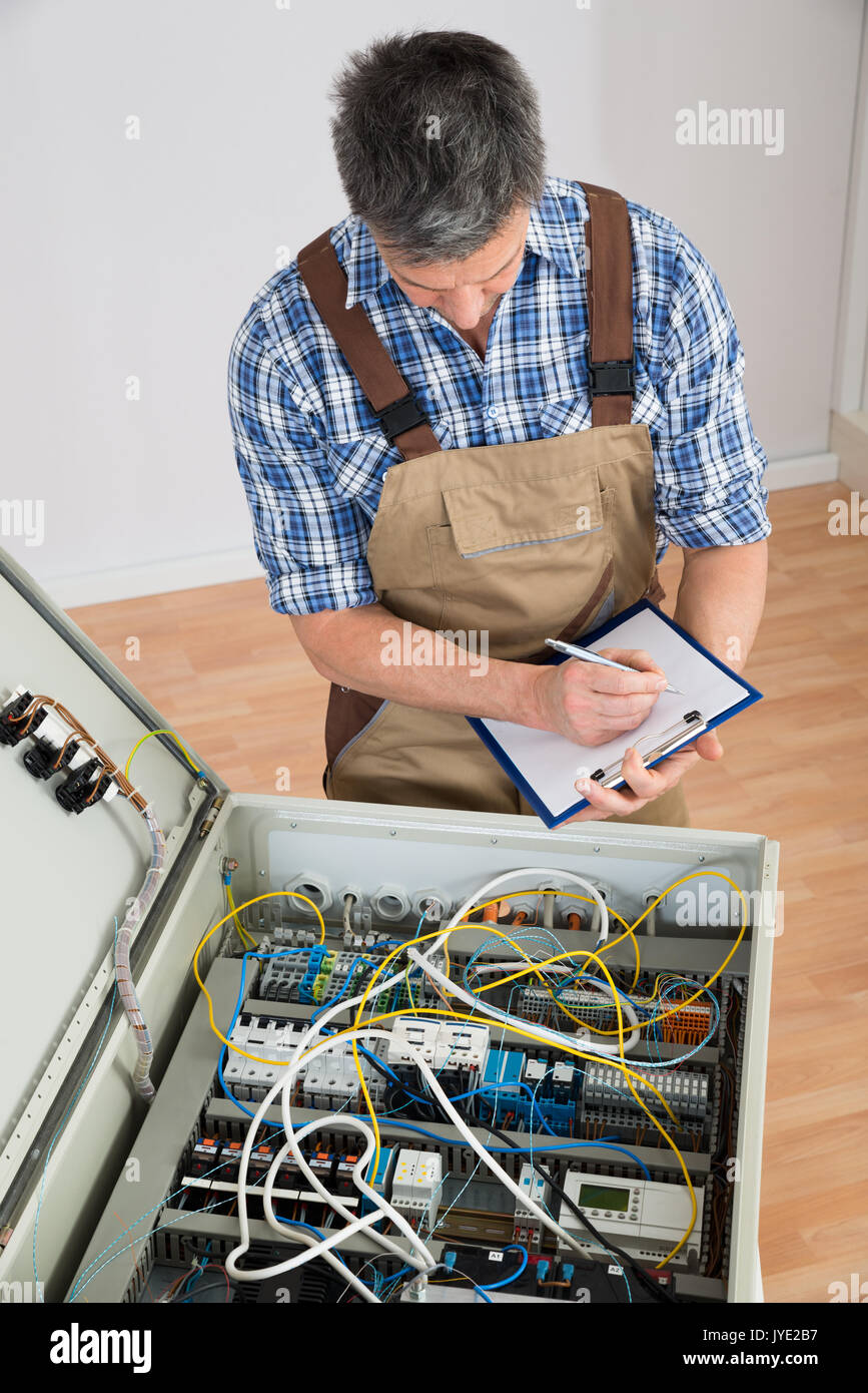Electrician Looking At Fuse Box Holding Clipboard Stock Photo