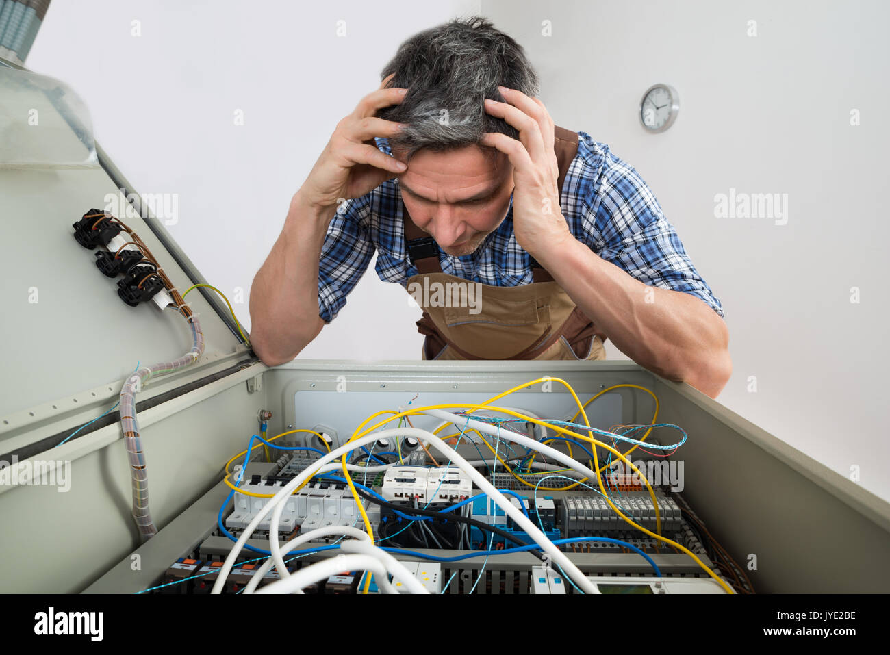 Portrait Of A Confused Electrician Looking At Fuse Box Stock Photo