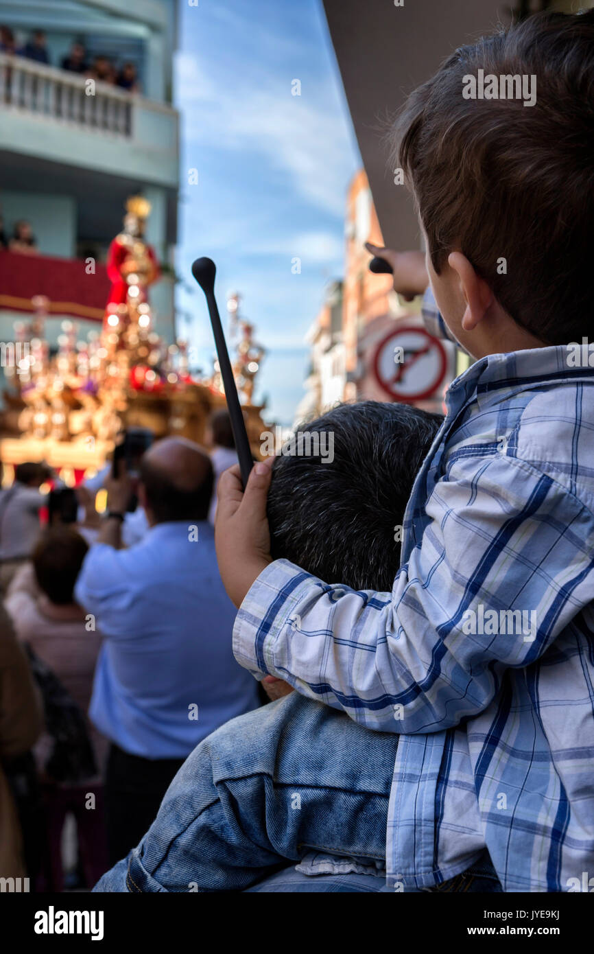 child of backs with ramrod of drum in his hand with his father during Holy week procession, Spain Stock Photo