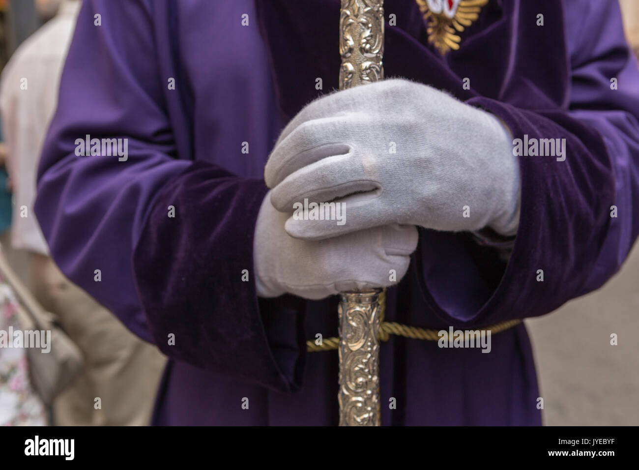 Penitent with purple velvet tunic supports support staff during atonement station in holy Friday, Linares, Andalusia, Spain Stock Photo