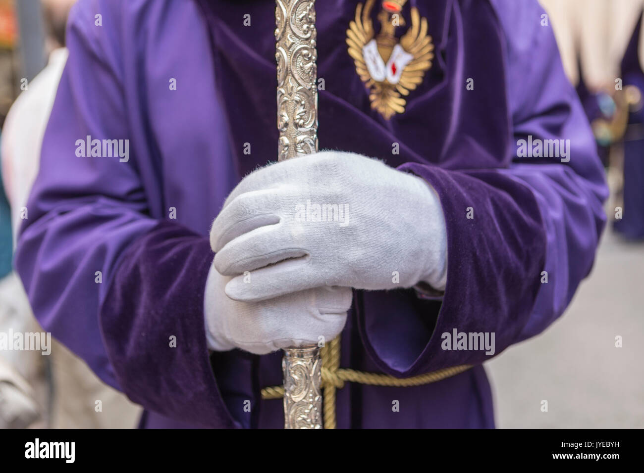 Penitent with purple velvet tunic supports support staff during atonement station in holy Friday, Linares, Andalusia, Spain Stock Photo