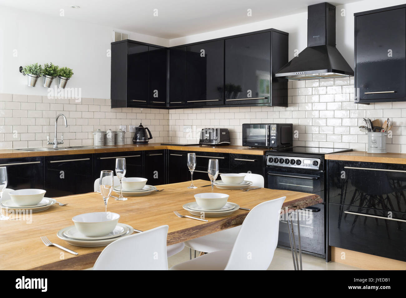 A modern kitchen with glossy black cabinets, solid oak worktops and a bespoke oak dining table. Stock Photo