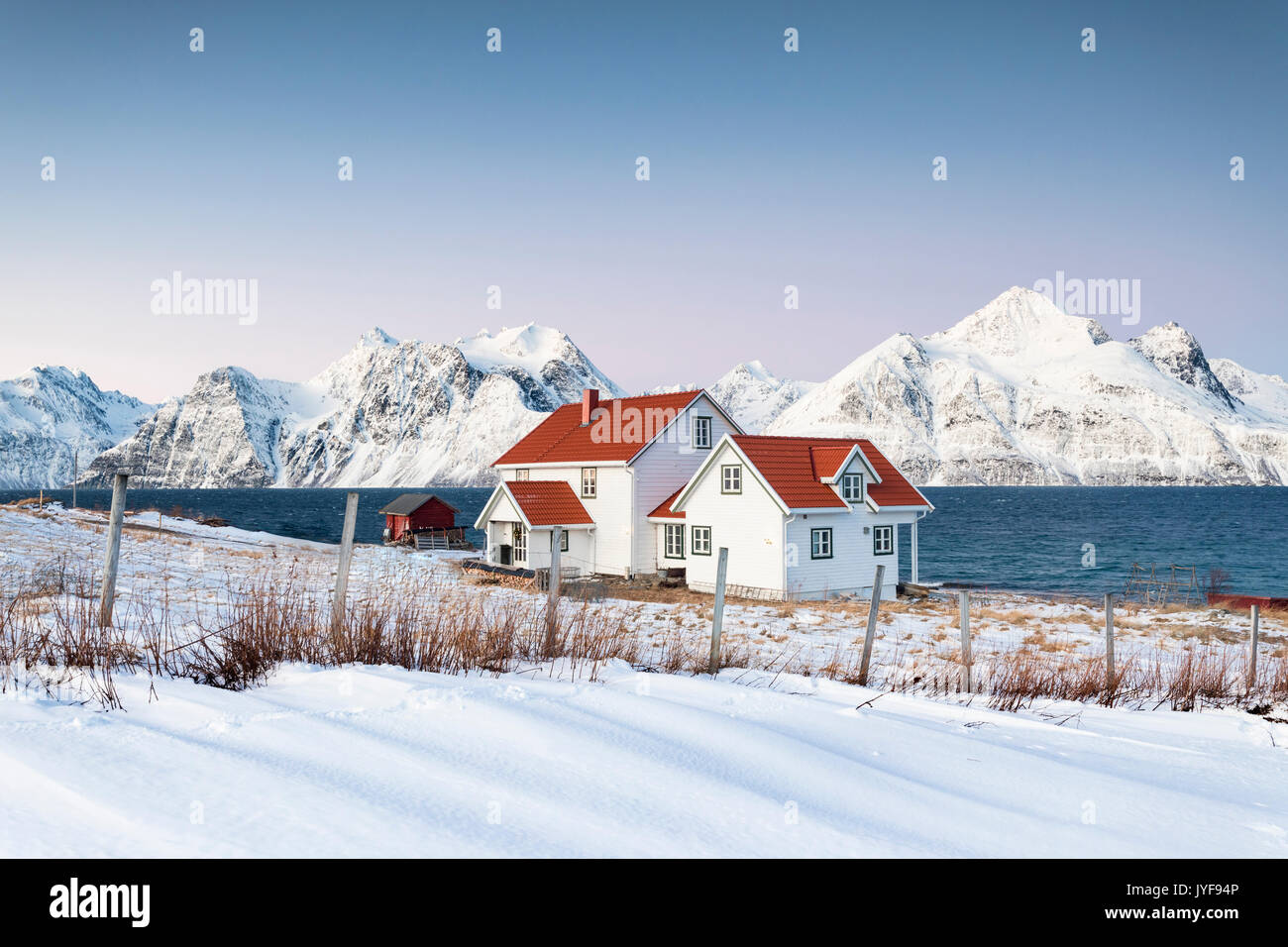 Blue sky on the wooden huts called Rorbu framed by frozen sea and snowy peaks Djupvik Lyngen Alps Tromso Norway Europe Stock Photo