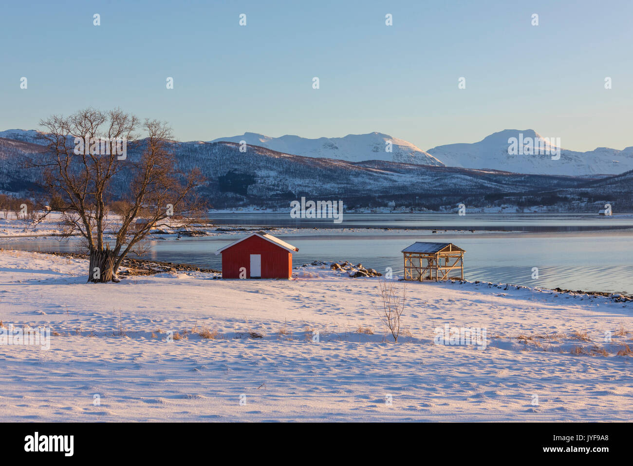 Wooden hut in the snowy landscape facing the cold sea on the road leading from Gibostad to Finnsnes Senja Tromso Norway Europe Stock Photo