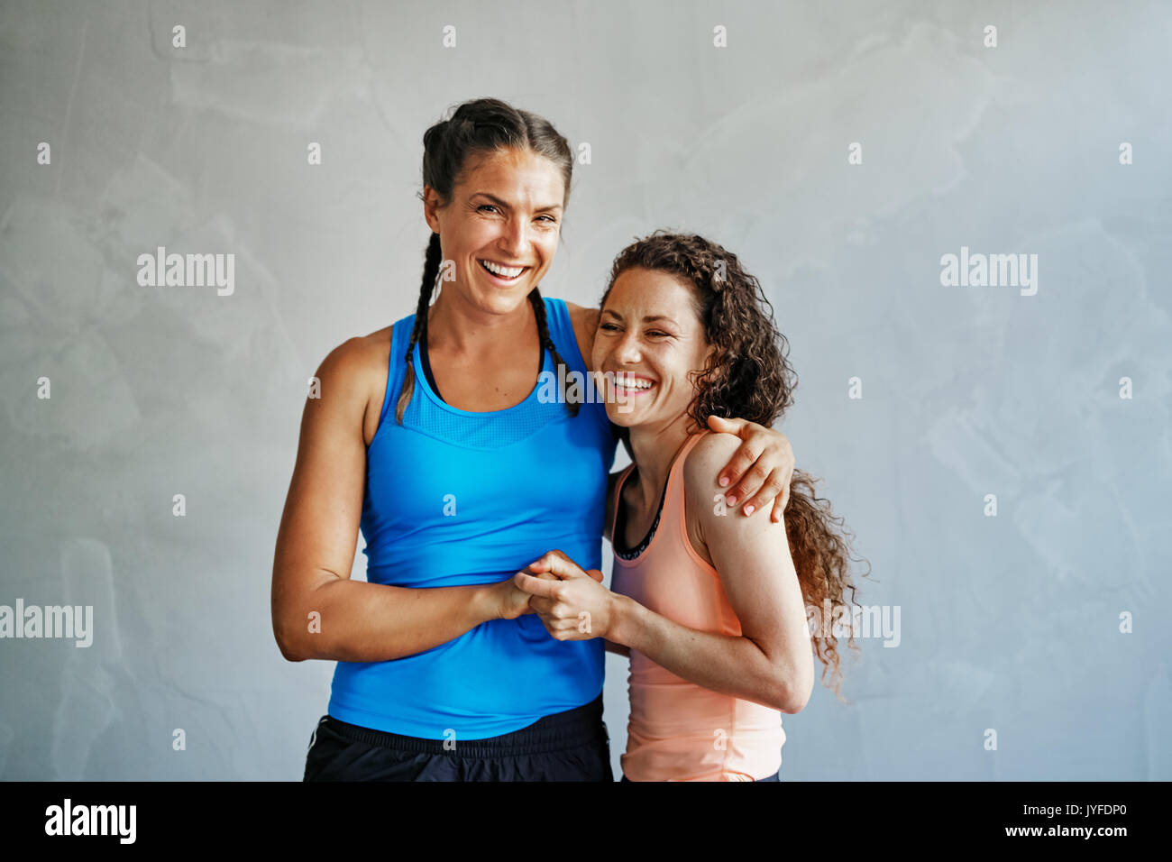 Two smiling young female friends in sportswear high fiving each other while doing pushups together on the floor of a gym Stock Photo