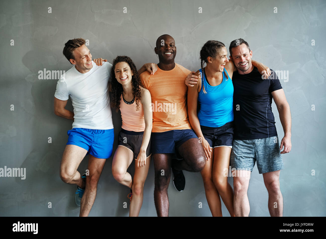 Smiling group of friends in sportswear laughing together while standing arm in arm in a gym after a workout Stock Photo