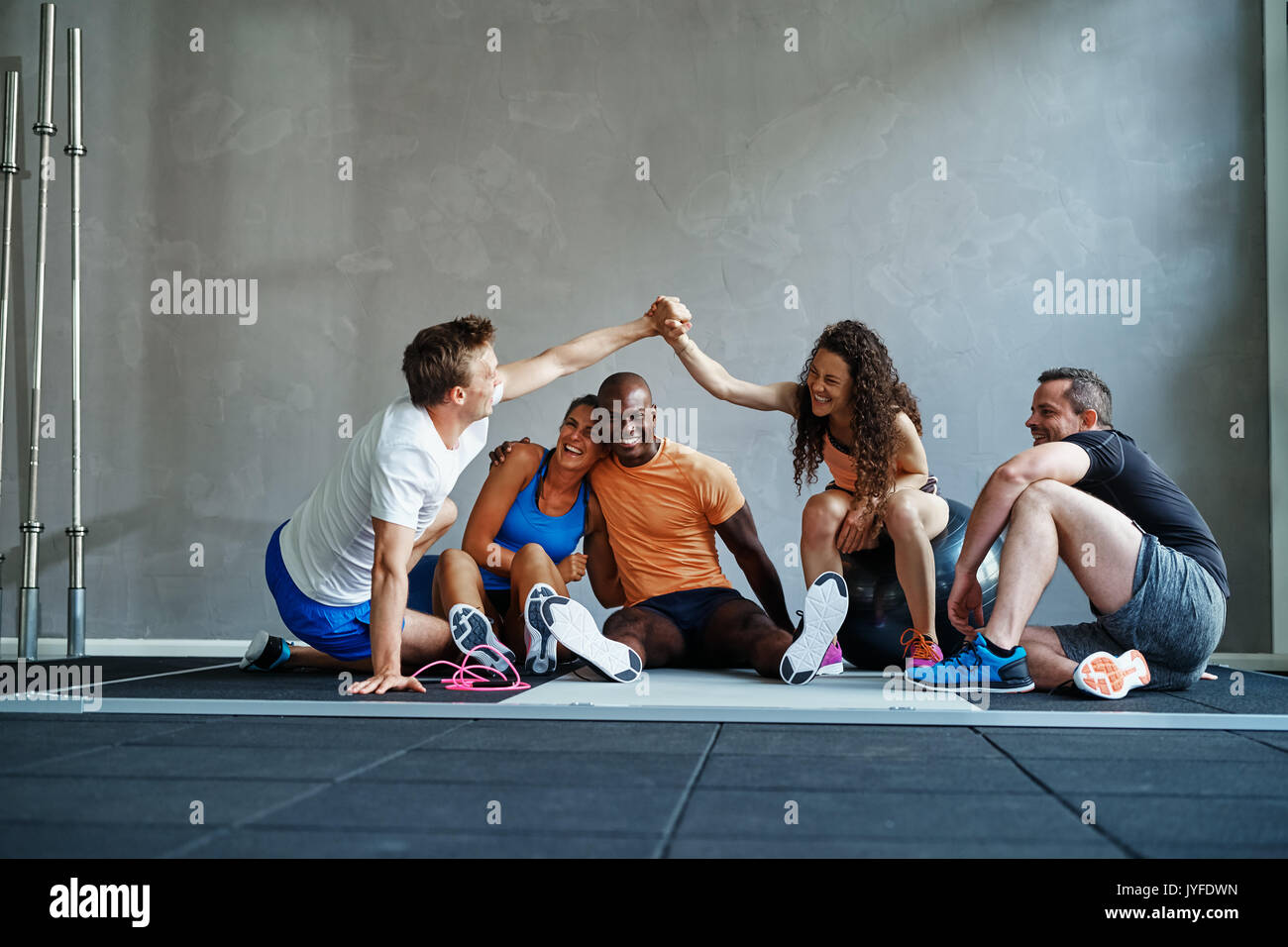 Two friends in sportswear high fiving each other while sitting on the floor of a gym talking with friends after a workout Stock Photo