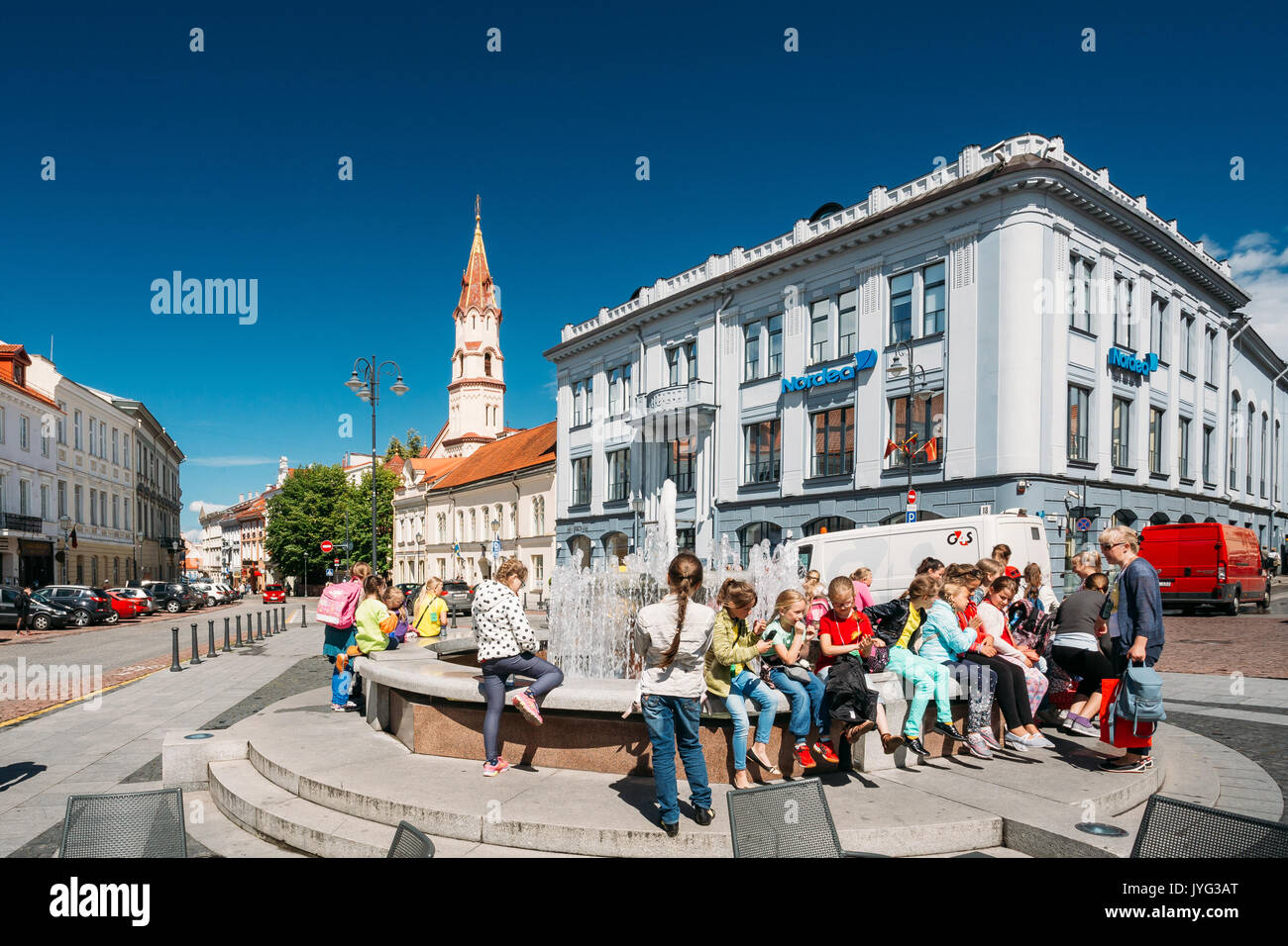 Vilnius, Lithuania - July 5, 2016: Children Resting Near Town Hall Square Fountain In Rotuses Square In Old Town. St. Nicholas Church In Sunny Summer  Stock Photo