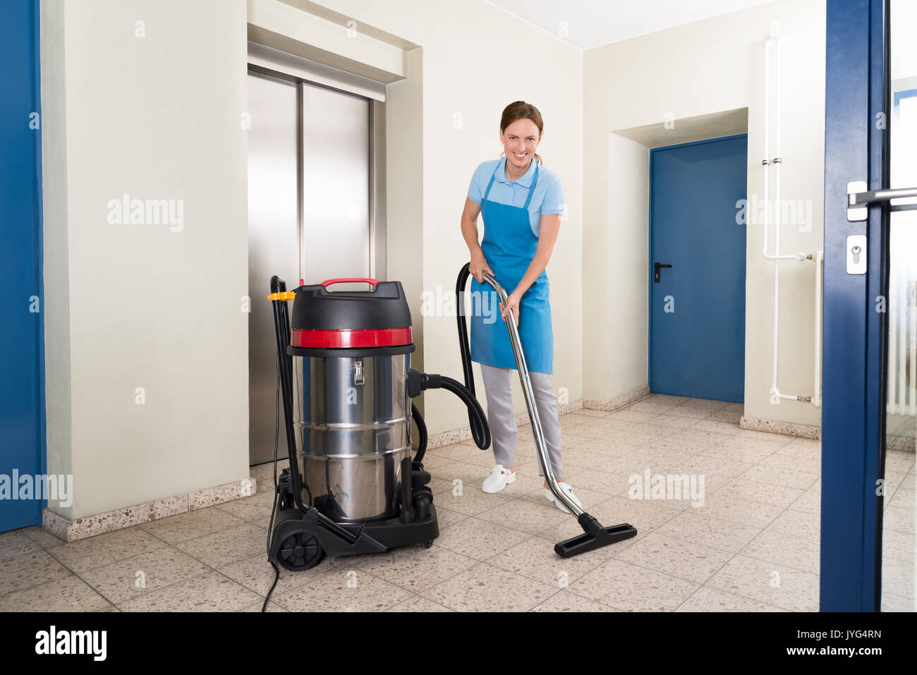 Young Female Janitor Cleaning Floor With Vacuum Cleaner Stock Photo
