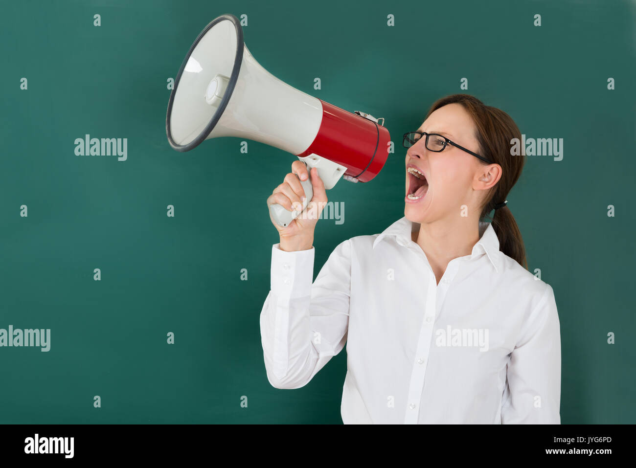 Young Businesswoman Shouting Though Megaphone Against Chalkboard Stock Photo