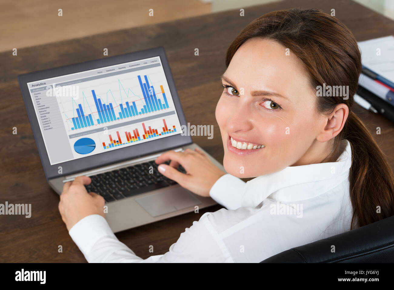 Happy Businesswoman Working With Graphs On Laptop At Desk Stock Photo