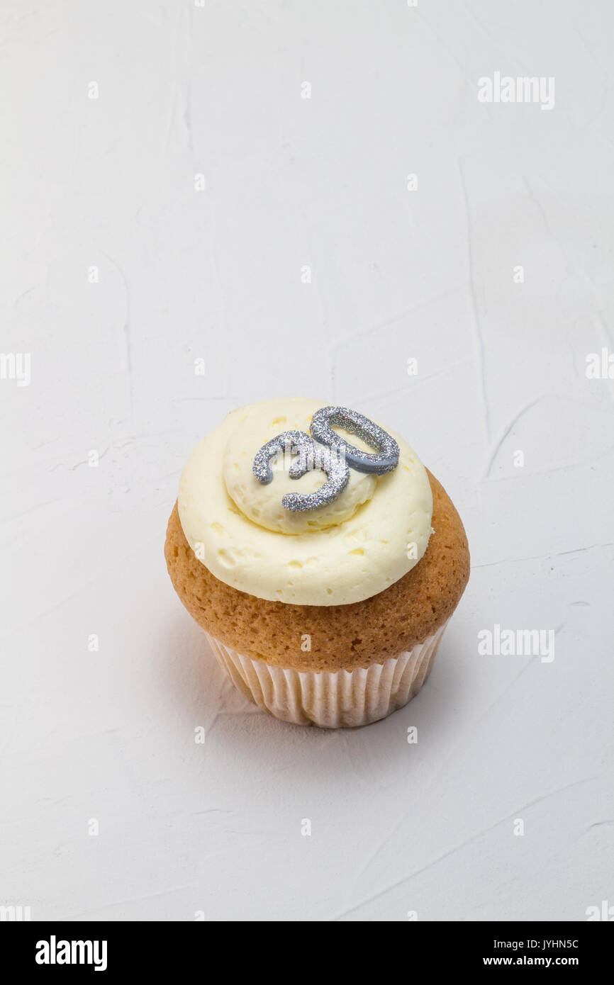 Single vanilla sponge cup cake with silver glitter number 30 on top of creamy white frosting isolated on rustic white background - celebration backgro Stock Photo