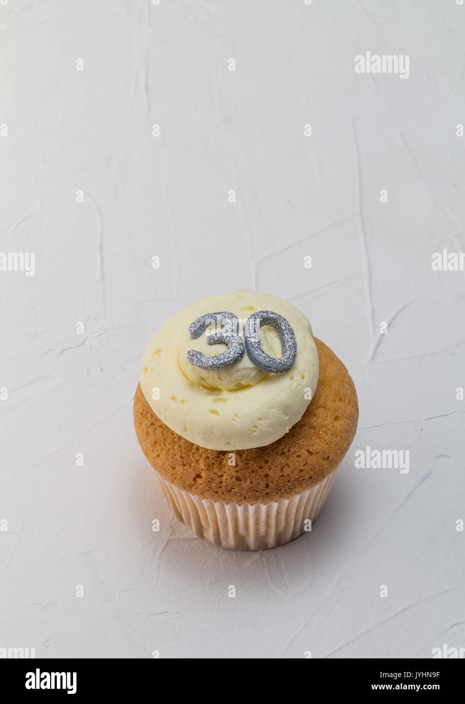 Single vanilla sponge cup cake with silver glitter number 30 on top of creamy white frosting isolated on rustic white background - celebration backgro Stock Photo