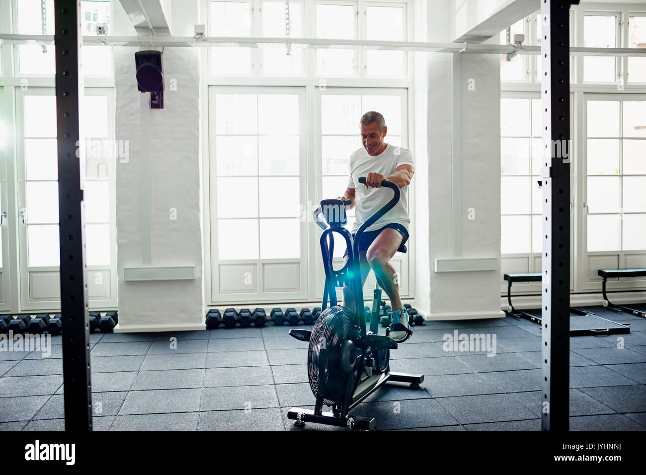 Smiling mature man in sportswear riding a stationary bike while working out alone at the gym Stock Photo
