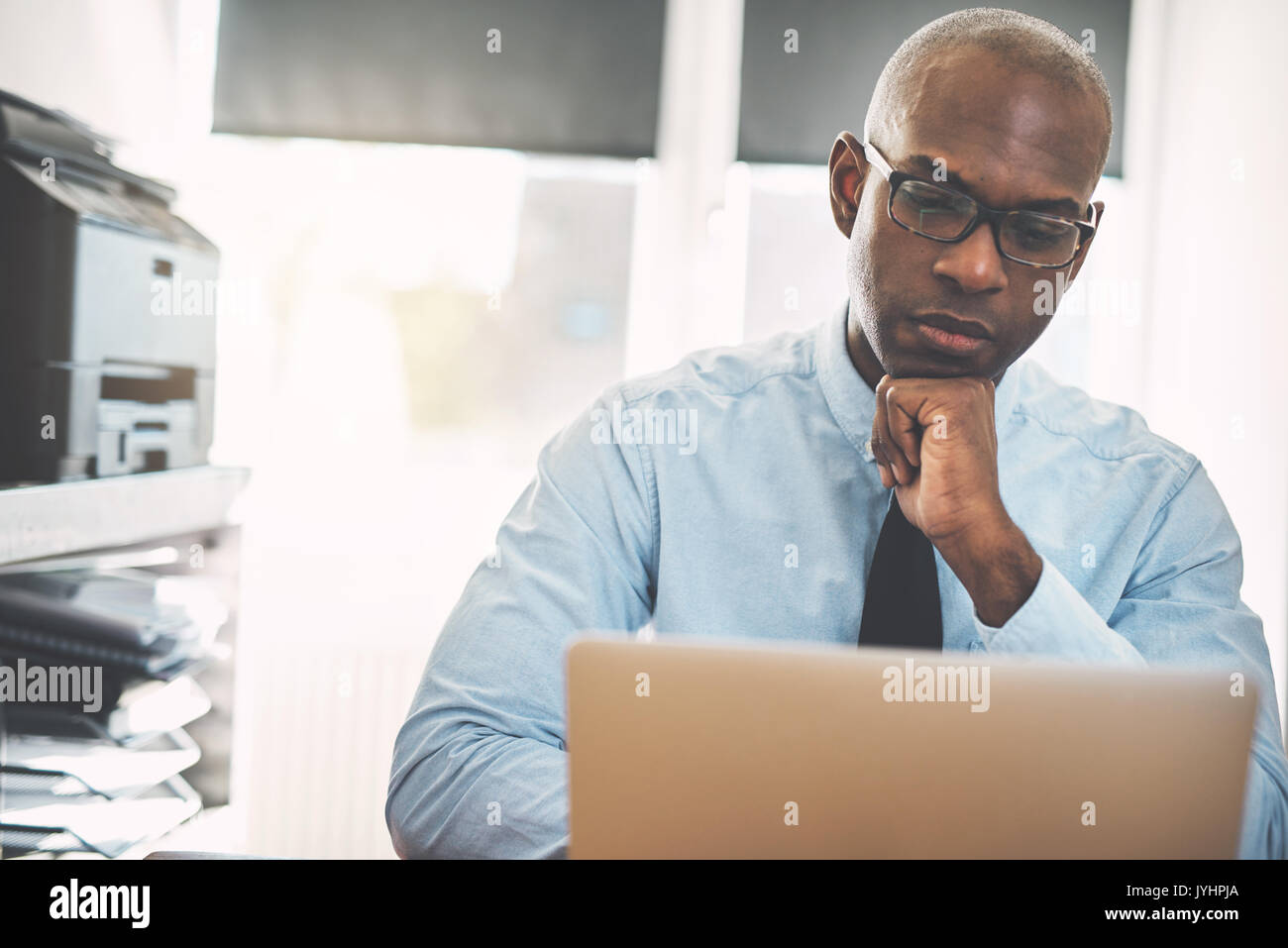 Focused African entrepreneur deep in thought while sitting at a desk working online with a laptop from his home office Stock Photo