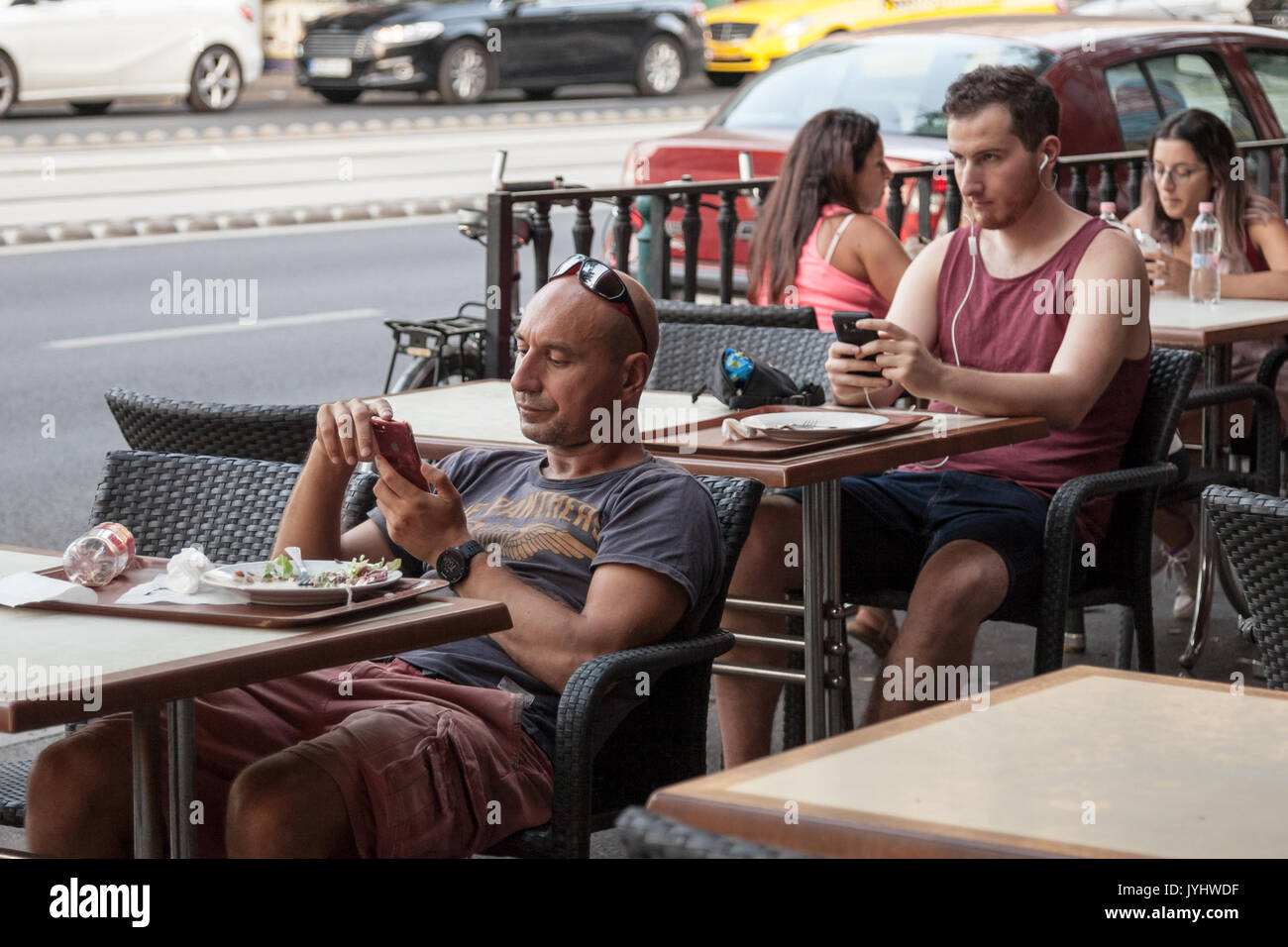 BUDAPEST, HUNGARY - AUGUST 11, 2017: two young caucasian men using their smartphones while sitting at bar tables in the center of Budapest, Hungarian  Stock Photo