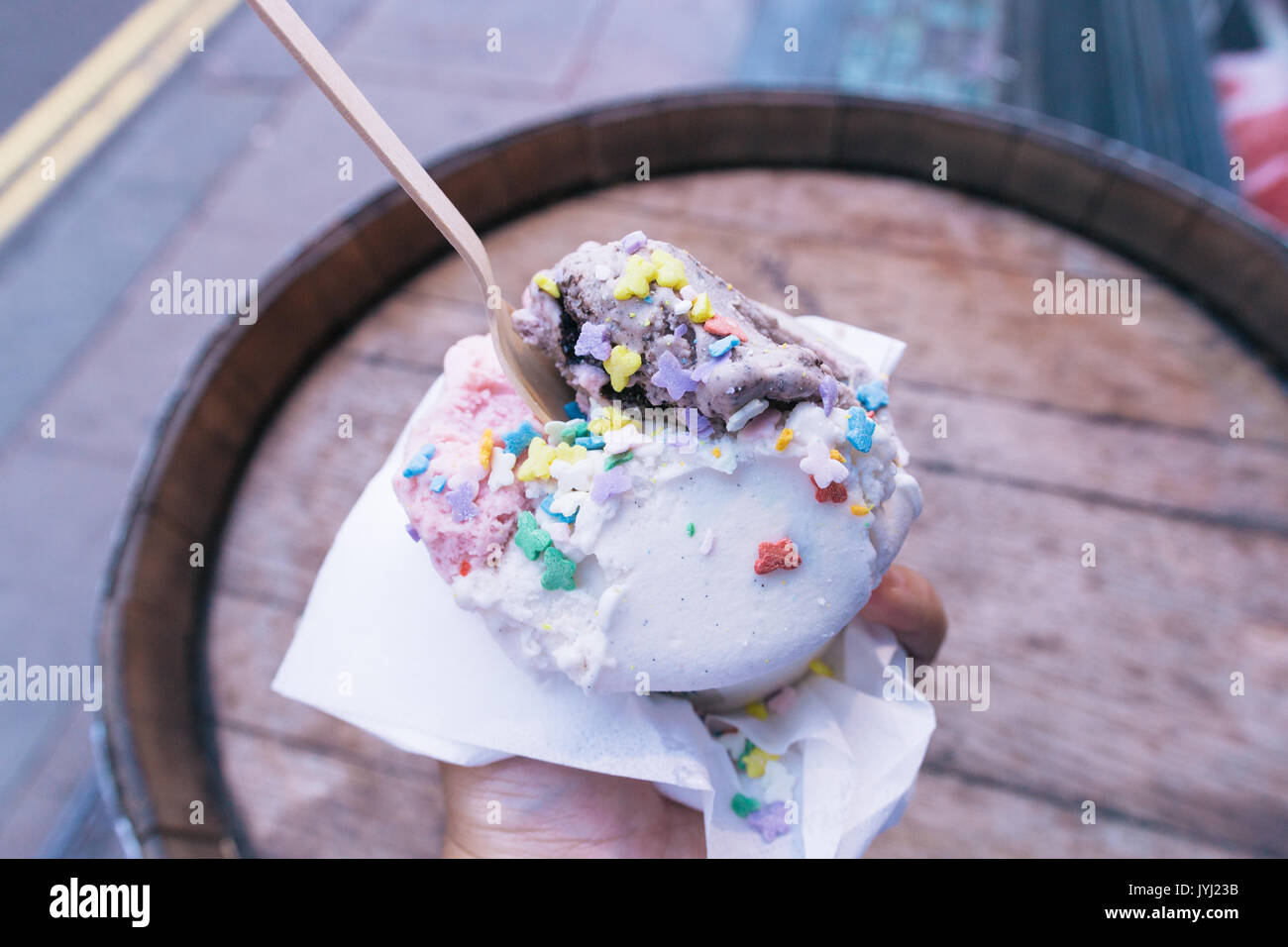 Vegan Ice Cream cone with sprinkles and wooden fork in front of wooden barrel table Stock Photo