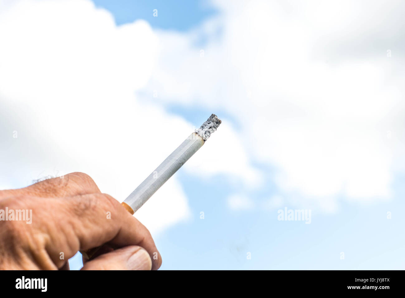 Man Holding a Lit Cigarette Against a Cloudy Blue Sky Stock Photo
