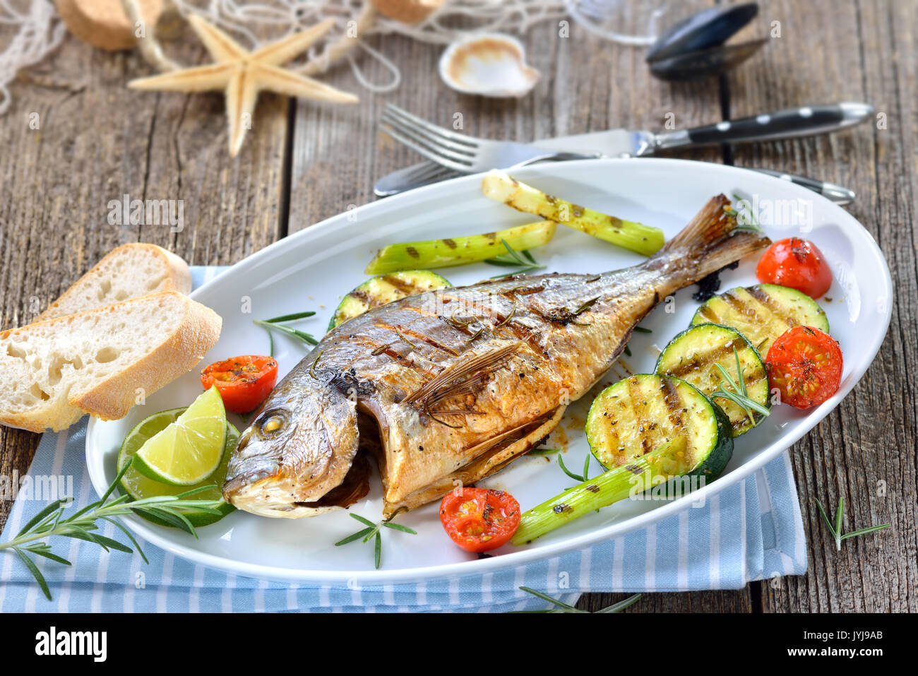 Grilled gilthead seabream with mixed rosemary vegetables served on an oval  white fish plate Stock Photo - Alamy