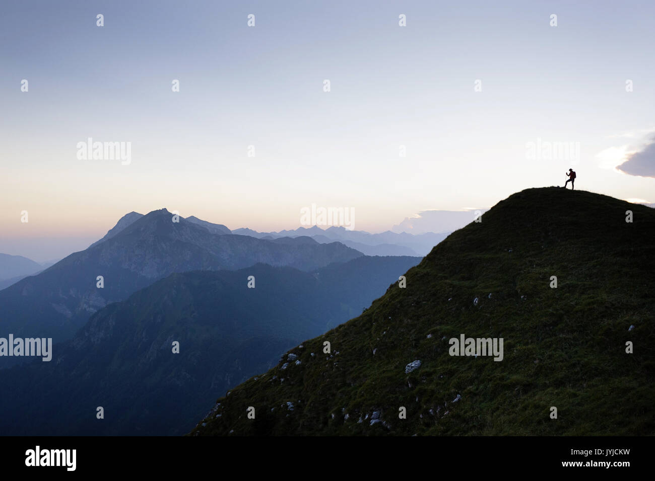 A silhouette of a woman standing on top of the mountain at twilight ...