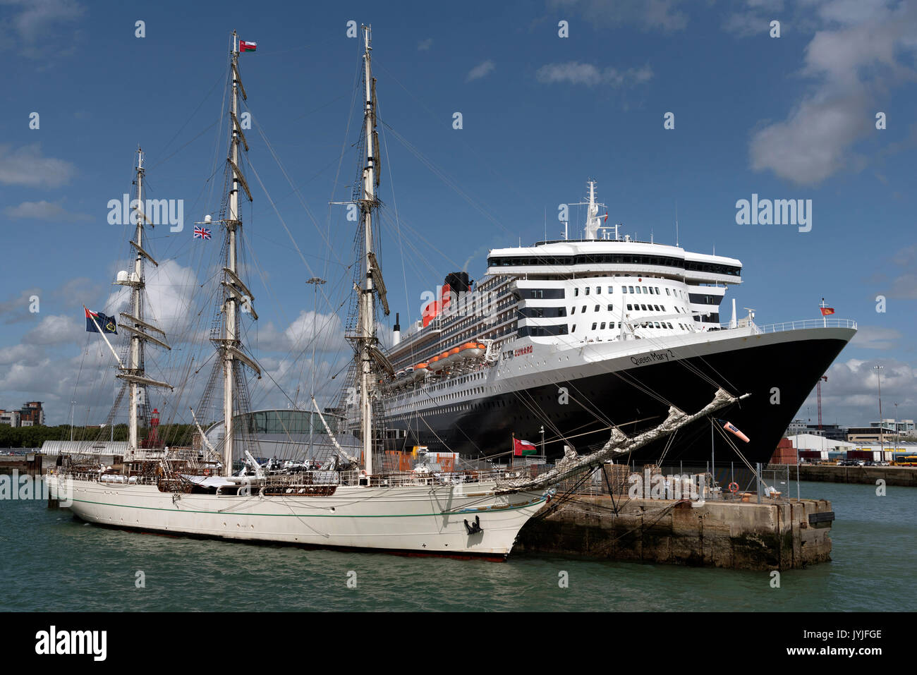 Shabab Oman II a full rigged training ship of the Royal Navy of Oman dwarfed by Cunard's Queen Mary 2 in Southampton Docks UK August 2017 Stock Photo