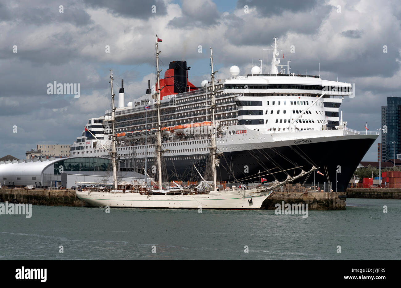 Shabab Oman II a full rigged training ship of the Royal Navy of Oman dwarfed by Cunard's Queen Mary 2 in Southampton Docks UK August 2017 Stock Photo