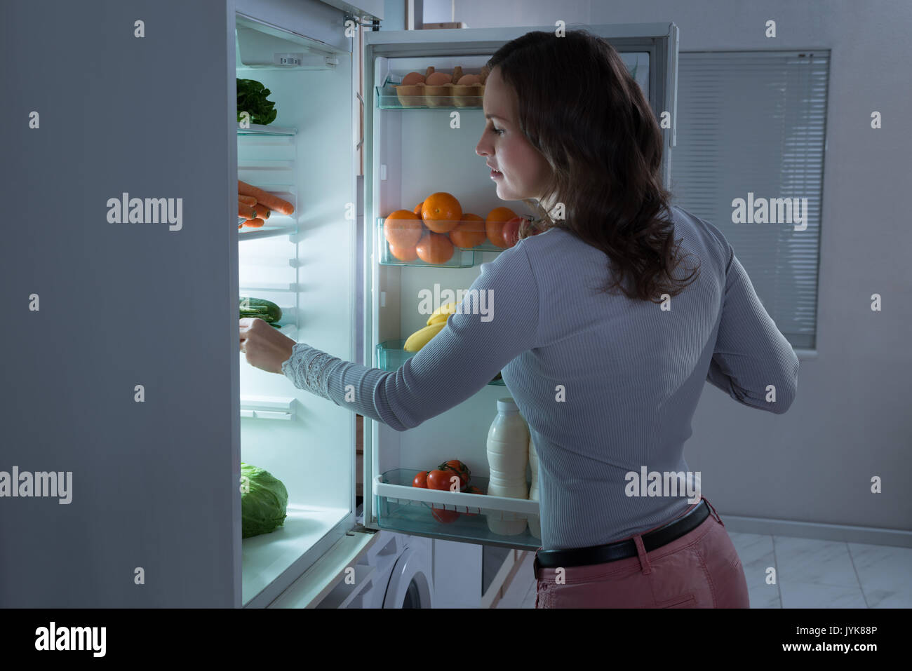 Young Beautiful Woman Searching For Food In The Fridge Stock Photo