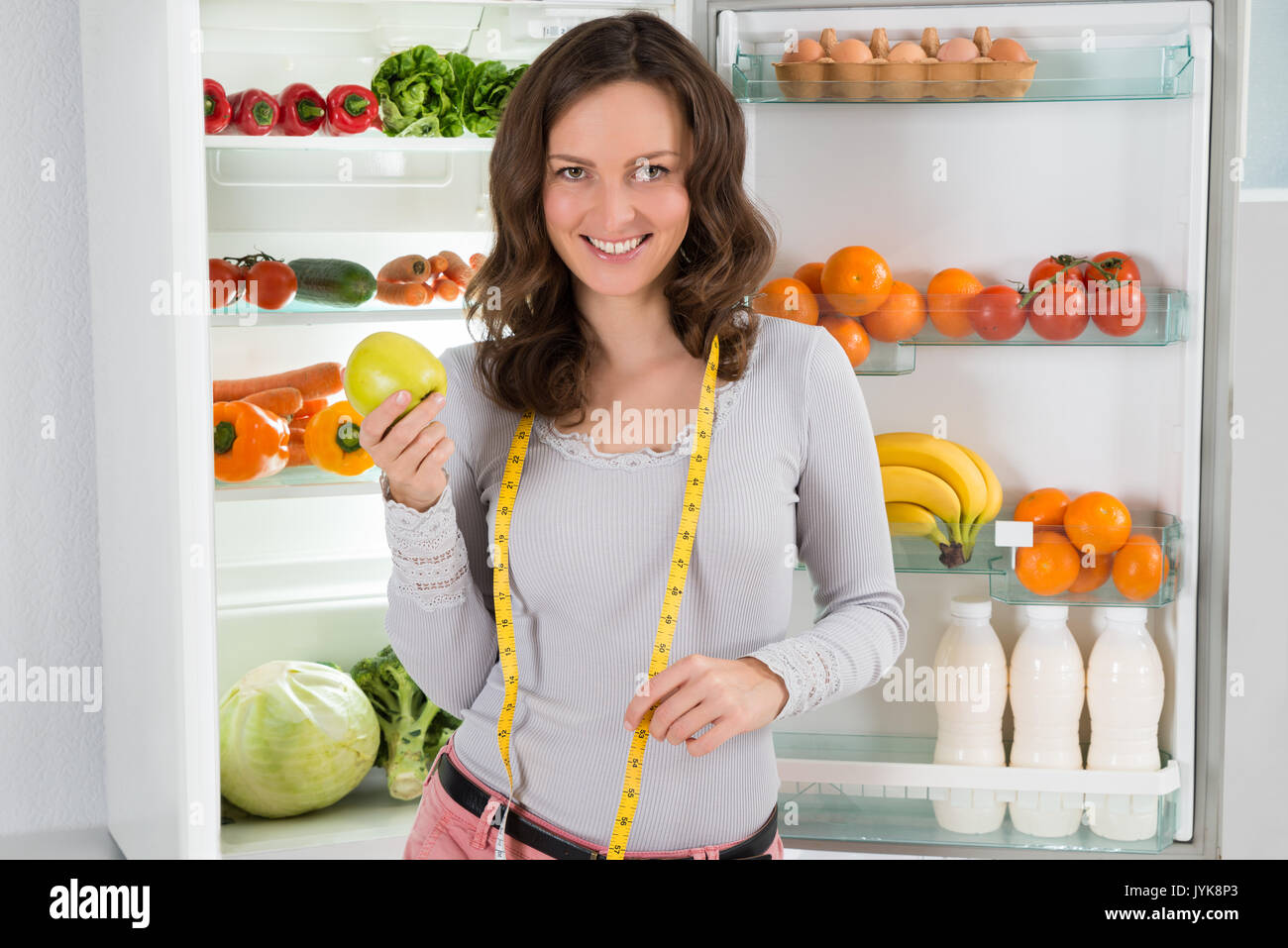 Happy Woman With Measuring Tape And Green Apple Near The Open Refrigerator With Healthy Food Stock Photo
