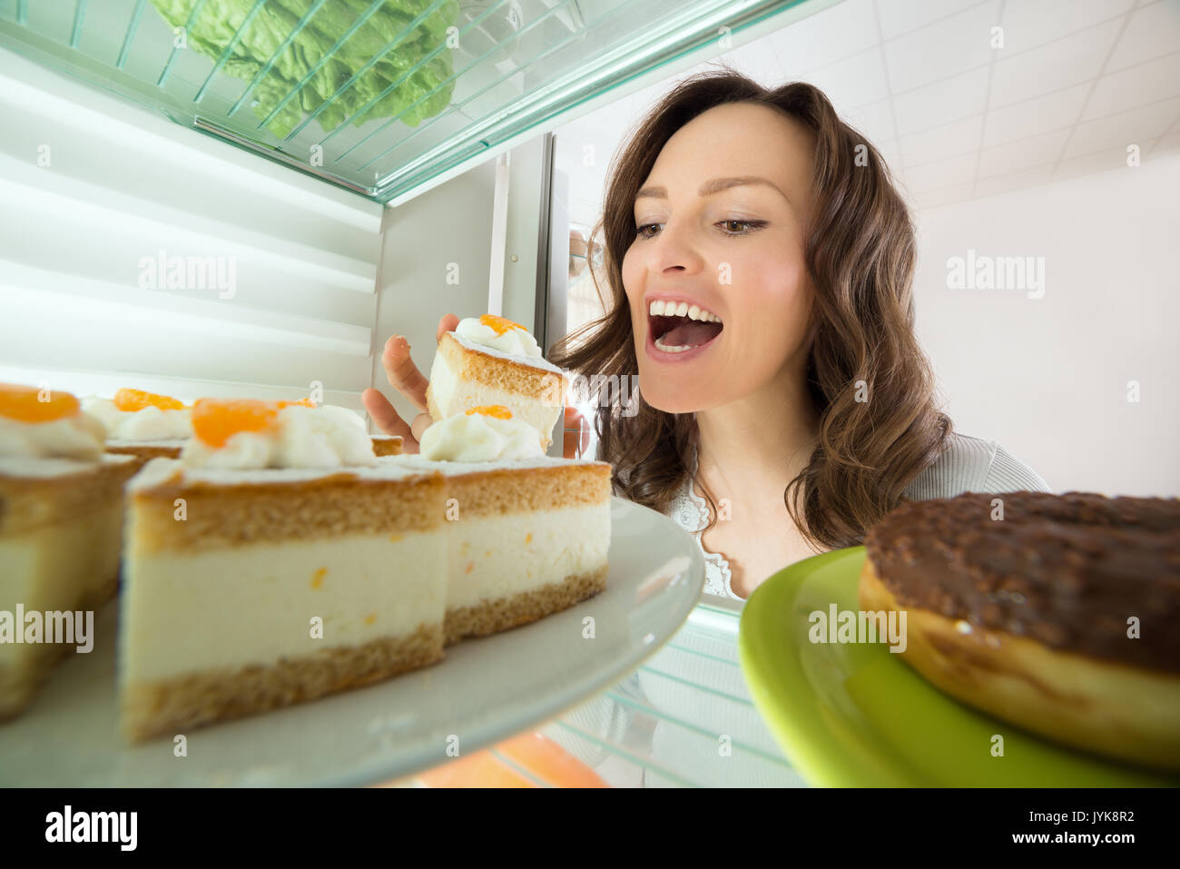 Hungry Young Woman Eating Slice Of Cake From Fridge At Home Stock Photo