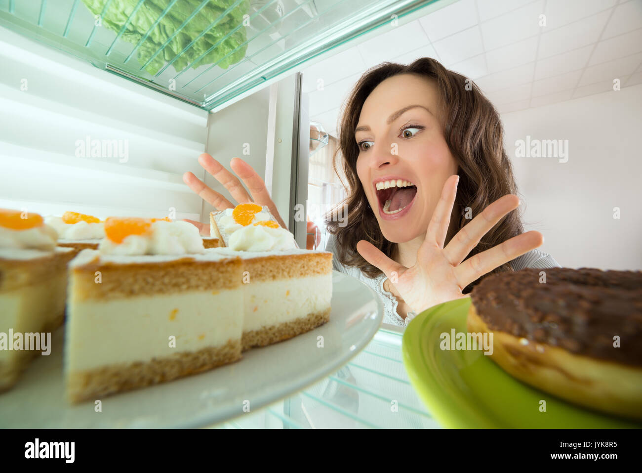 Excited Young Woman Looking At Cake In Refrigerator At Home Stock Photo