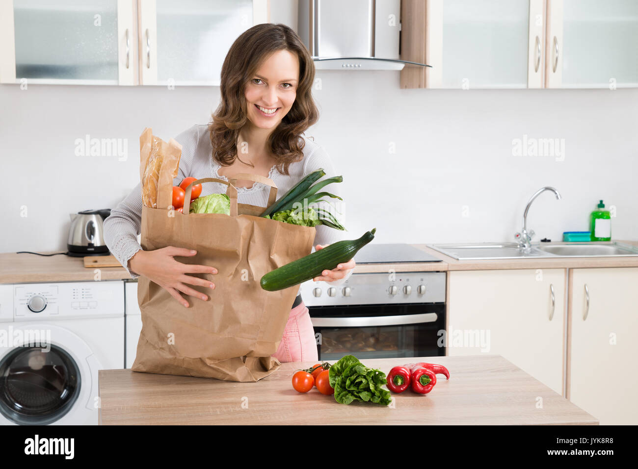 Happy Woman Sorting After Purchasing Vegetables In Kitchen Stock Photo