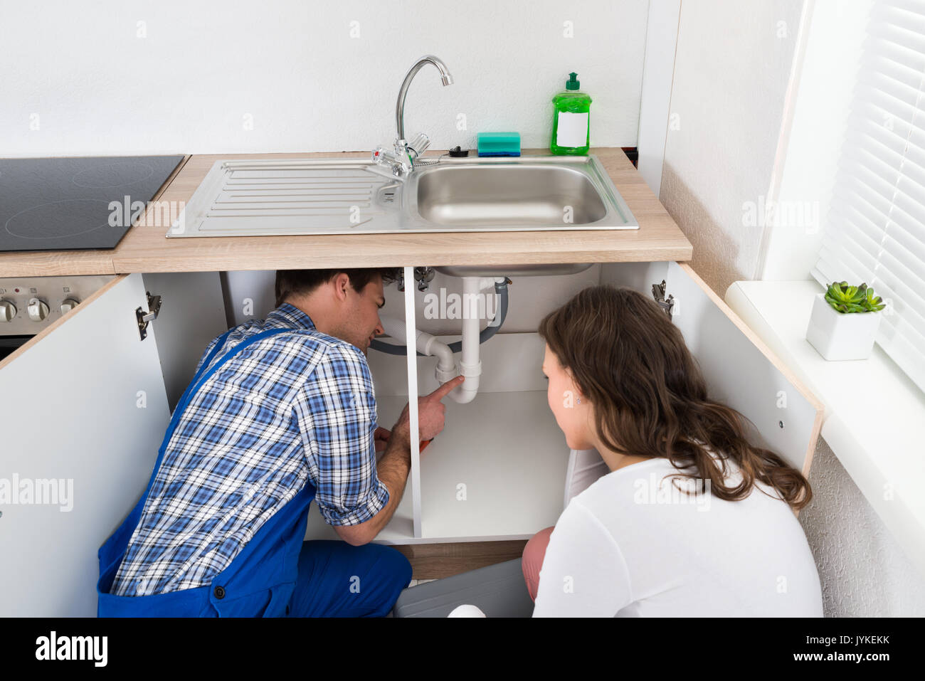 Plumber Showing Damage In Sink Pipe To Woman Plumber At Home Stock