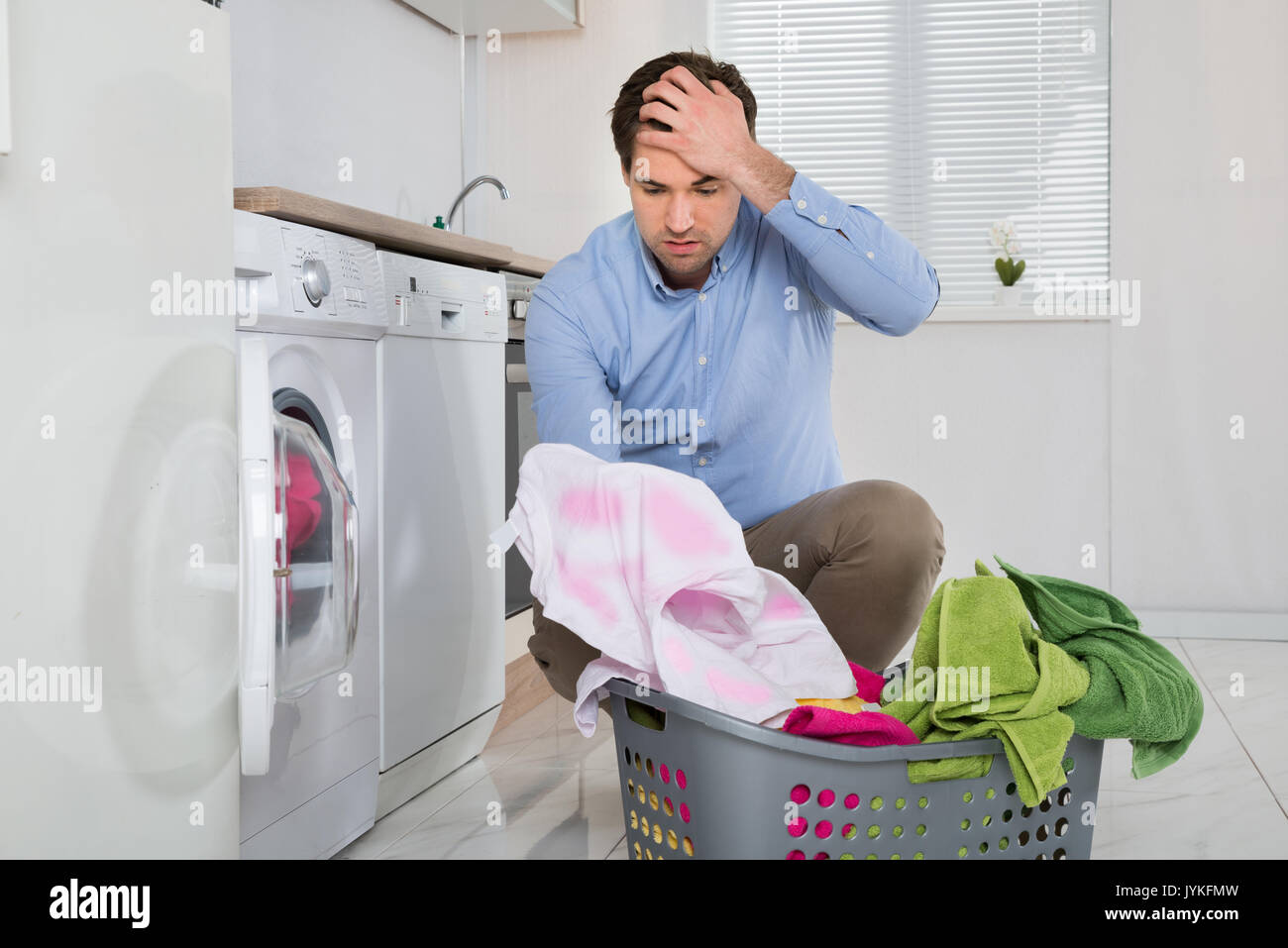 Man Near The Washing Machine With Laundry Basket Holding Stained Cloth In Kitchen Stock Photo