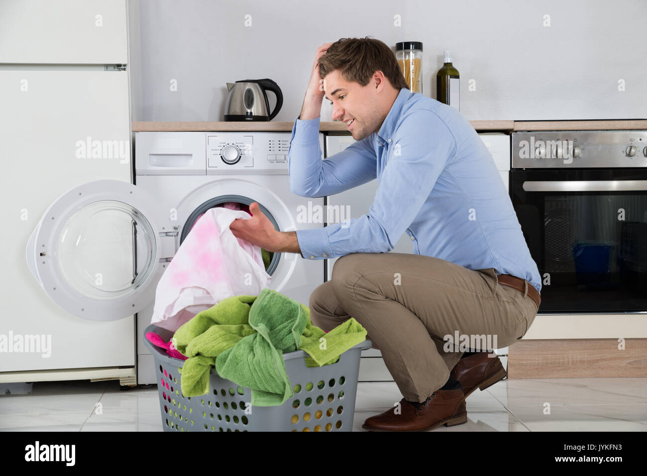 Man Near The Washing Machine With Laundry Basket Holding Stained Cloth In Kitchen Stock Photo