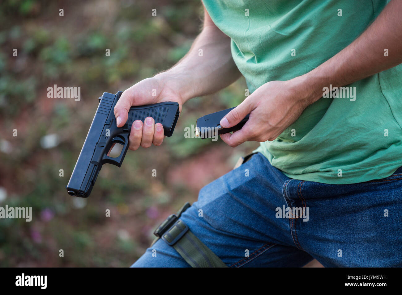 Guy with the pistol gun glock desert eagle changing bullets in the magazine to shot in the nature and having gun socket on the leg Stock Photo