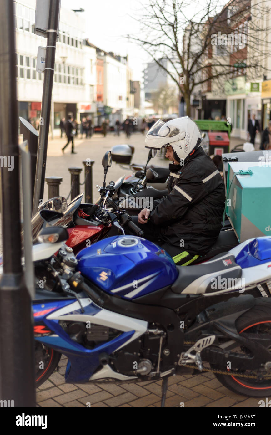 courier motorcycle helmet Motorbike courier sitting on a motorcycle with his helmet on resting with  other parked machines Stock Photo