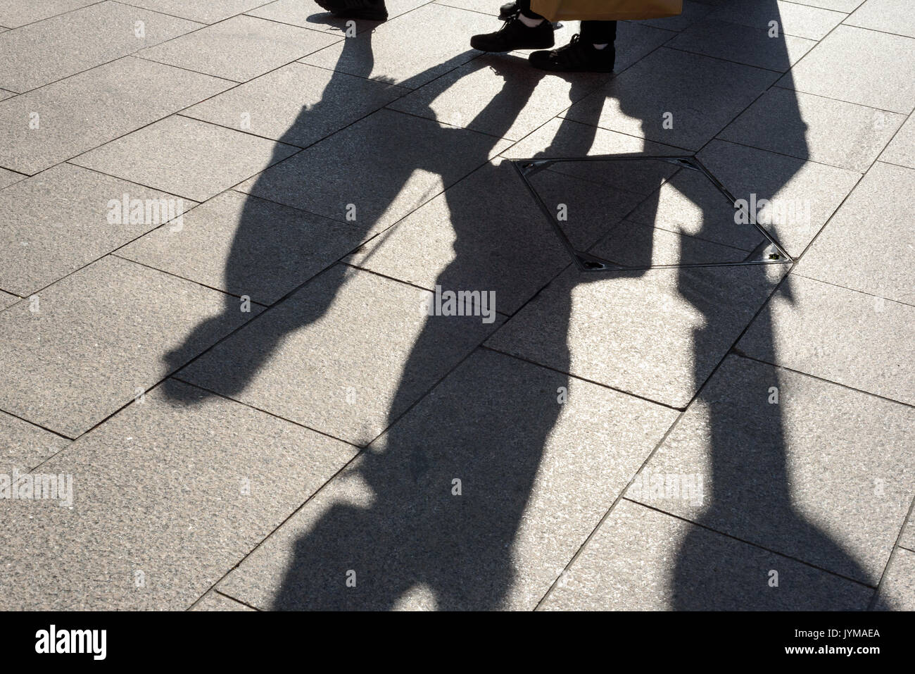 Two peoples legs and body in strong shadow on a tiled pavement in daylight Stock Photo