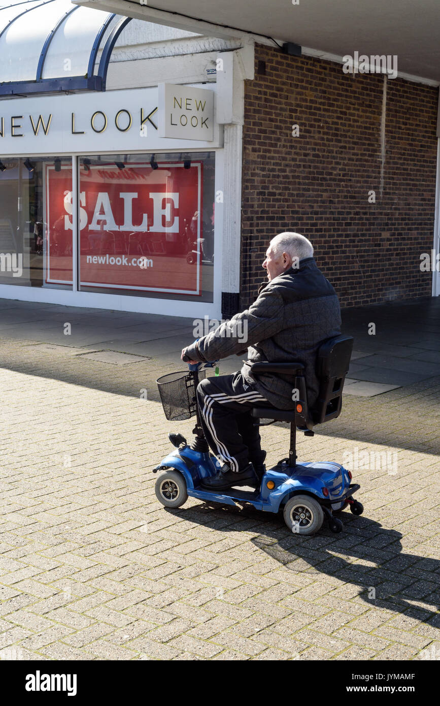 Elderly old man sits and rides on a mobility Scooter in a shopping area in Witham Essex England Stock Photo