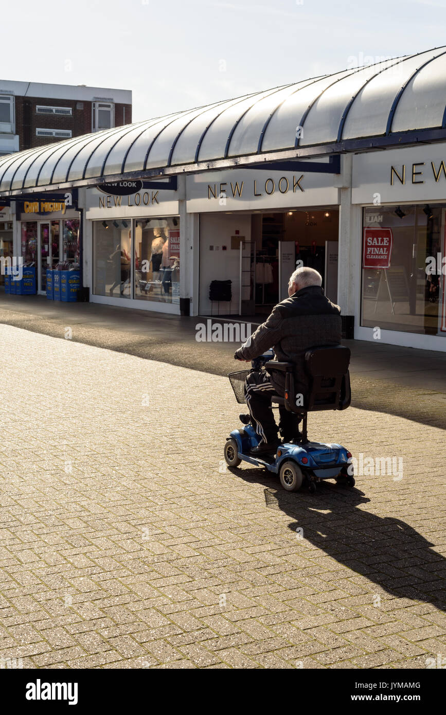 Elderly old man sits and rides on a mobility Scooter in a shopping area in Witham Essex England Stock Photo