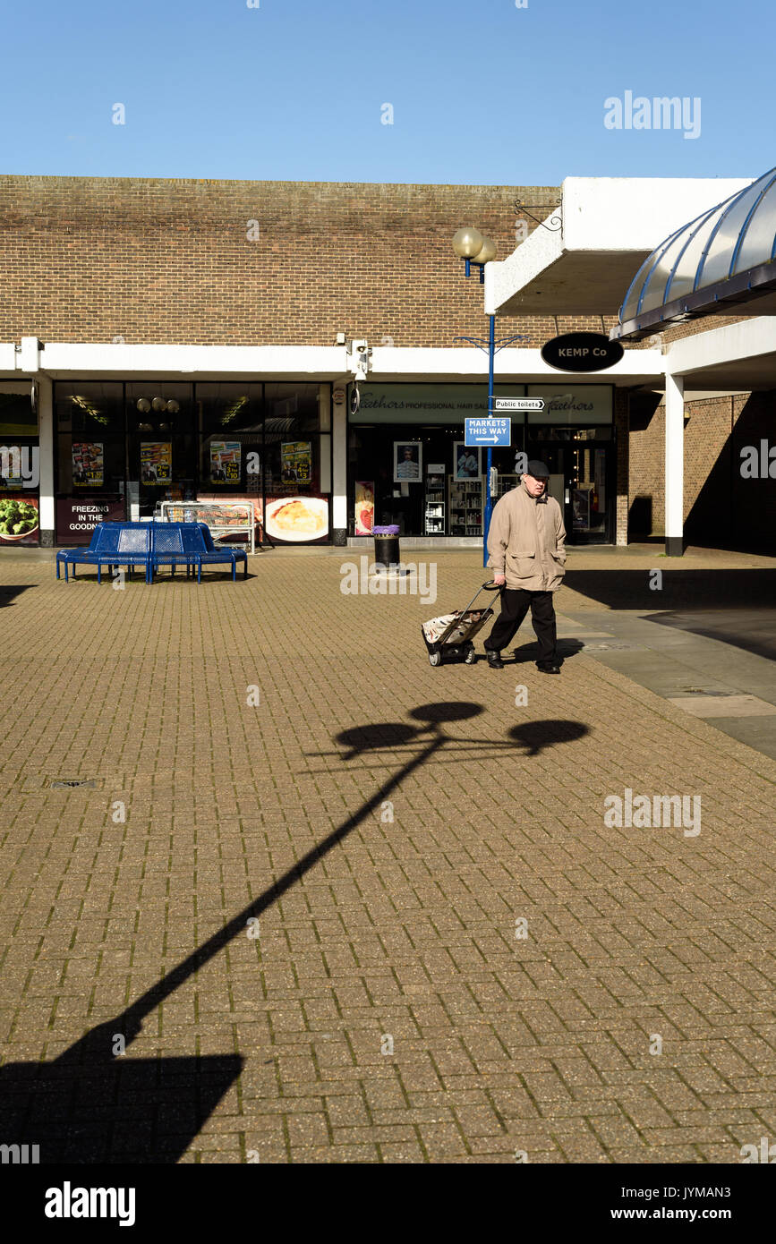 Single oap pensioner pulling a shopping trolley walks alone through an empty shopping center in the day in the outside sunshine Stock Photo