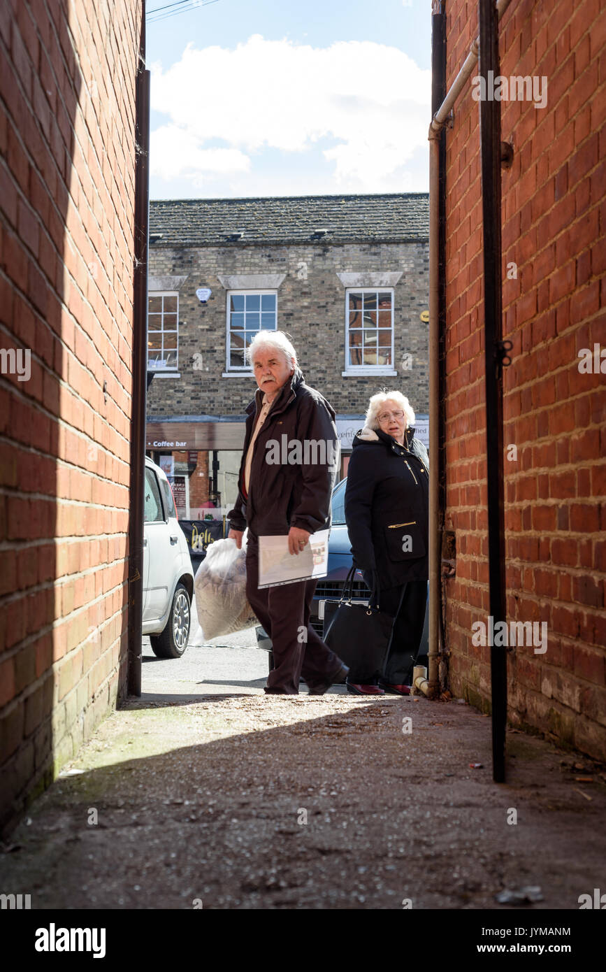 Elderly people peering down a  darkened alleyway in shadow staring directly towards the photographer in daylight on a typical average high-street in E Stock Photo