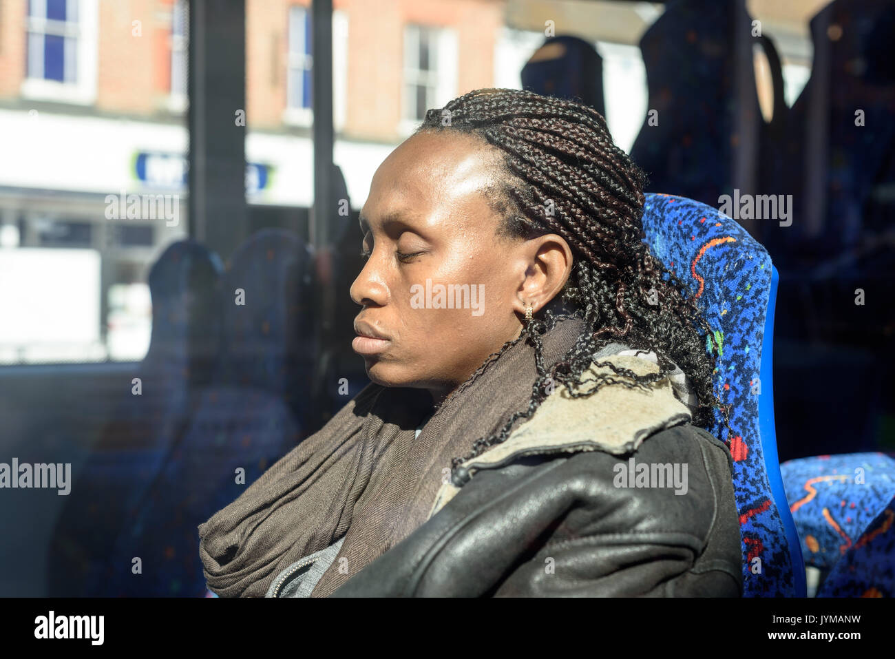 Sleepy black woman with dreadlocks hair sitting on a bus in bright sunshine Stock Photo