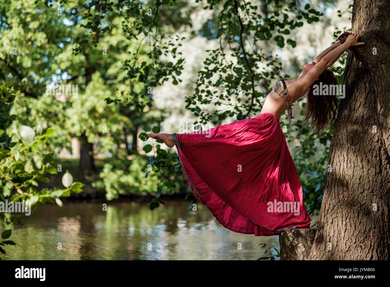 Caucasian woman in forest holding tree doing yoga asana Stock Photo