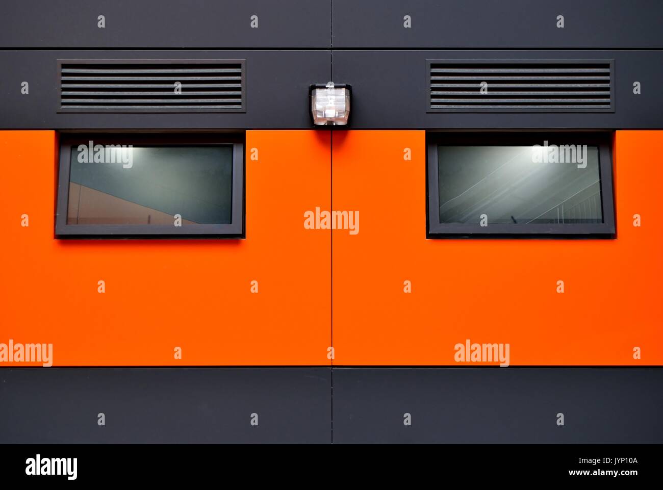 Front view exterior of modern office with tinted windows, gray steel sunshades and orange steel cladding as abstract background with space for copy. Stock Photo